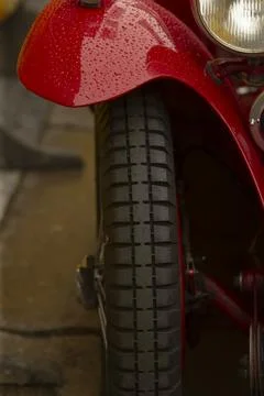 Closeup motorcycle front tyre, red fender and rain droplets on wet tread wheel Stock Photos