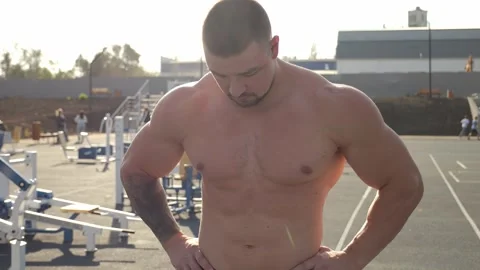 Closeup of a muscular man with a bare torso on an outdoor sports field at sunset Stock Footage 315093636