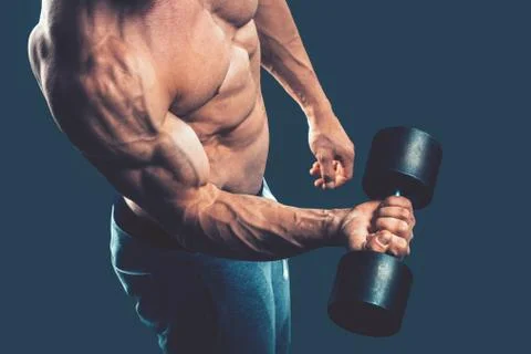 Closeup of a muscular young man lifting dumbbells weights on dar Stock Photos