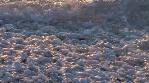 Closeup of ocean waves on white pebbles beach at sunset Stock Footage 259837560