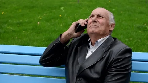 Closeup of Old man sitting on the bench in the park and talking on cellphone Stock Footage 72076642