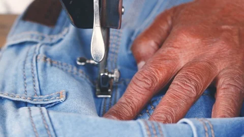 Closeup of old man's hands sewing blue jeans with a sewing machine Stock Footage 120495781
