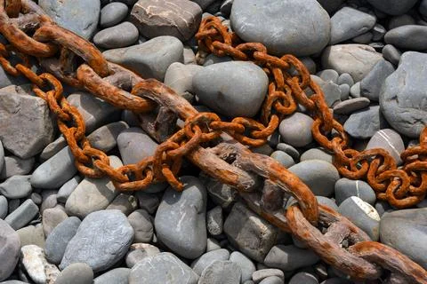 Closeup of old rusty iron links of a chain on a pebble beach for use as a b.. Stock Photos