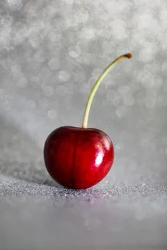 Closeup one red cherry fruit with root on light grey background with bokeh 스톡 사진