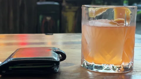 Closeup - Orange drink next to man's wallet at outdoor restaurant table Stock Footage 220567590