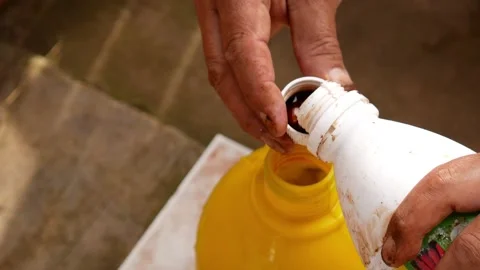 Closeup overhead shot of a man’s hand pouring a capful of liquid fertilizer Stock Footage 231973571