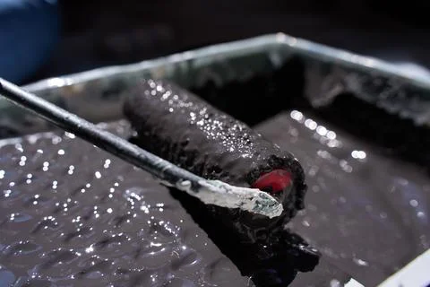 Closeup of paint roller covered with dark paint inside tray Stock Photos