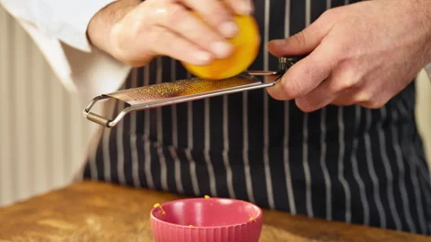 Closeup of pastry maker shredding bright yellow orange peel onto wooden board Stock Footage 324787522