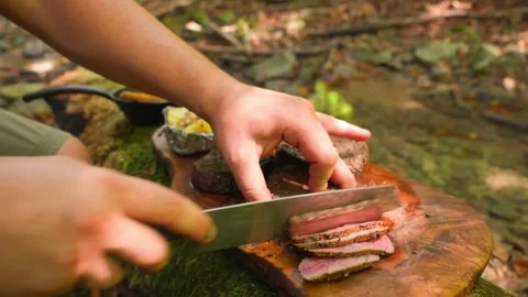 Closeup of a person slicing a cooked steak on a wooden board in the forest Stock Footage 336656796