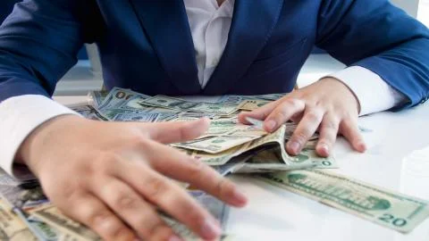Closeup photo of greedy businessman grabbing money lying on office desk Stock Photos