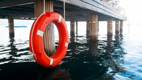 Closeup photo of red saving ring hanging wooden pier. Safety on sea water Stock-Fotos
