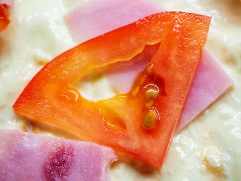Closeup photo of a triangular slice of red tomato and slices of ham lying on the Stock Photos