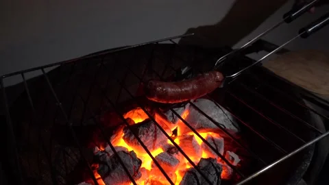 Closeup of a piece of chorizo moving it on a grill with charcoal and fire at Vidéo 155793543