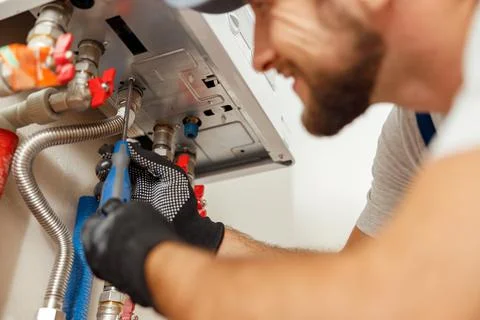 Closeup of plumber using screwdriver while installing new steel hot water Stock Photos
