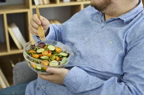 Closeup of plus size man holding fresh salad bowl with wooden fork at home Stock Photos