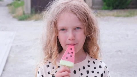 Closeup portrait of cute fair-haired curly caucasian girl eating watermelon ice Stock Footage 279550780