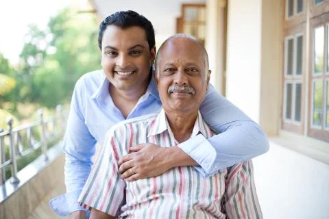 Closeup portrait, family, young man in blue shirt holding older man in stripe Stock Photos