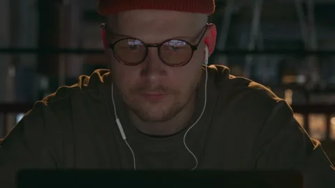 A closeup portrait of an IT programmer working in a dark cafe room on the laptop Stock Footage 260376771
