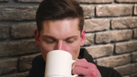 Closeup. Portrait of a man drinking coffee or tea from a white cup while taking Stock Footage 148384284
