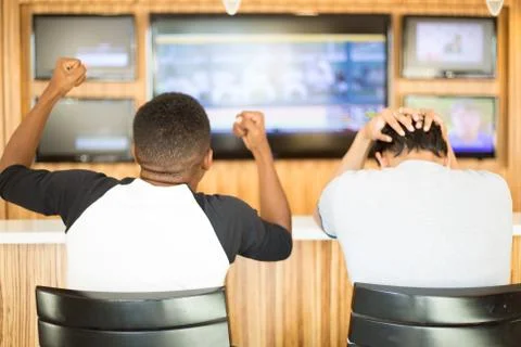 Closeup portrait, two men watching a sports game on tv.  one guy rejoices, ot Stock Photos