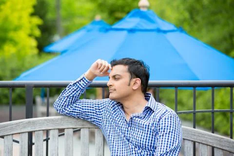 Closeup portrait, young man sitting on outside wooden bench, daydreaming Stock Photos