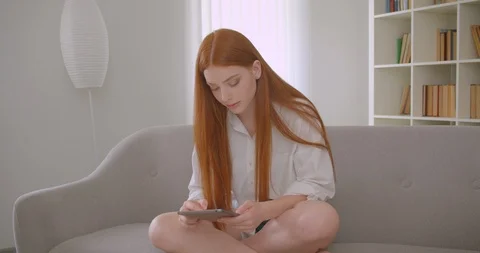 Closeup portrait of young pretty redhead female browsing the tablet sitting on Video stock 112667380