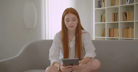 Closeup portrait of young pretty redhead female using the tablet sitting on the Video stock 112668101