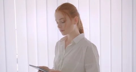 Closeup portrait of young pretty redhead female student using the tablet and Video stock 112676590