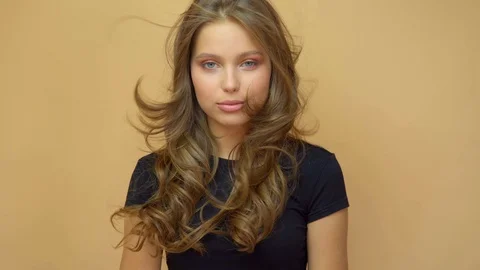 Closeup portrait of young wooman posing to a camera with blowed out hair on grey Stock Footage 114739374