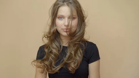 Closeup portrait of young wooman posing to a camera with blowed out hair on grey Stock Footage 114741004