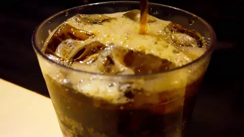 Closeup pouring brown root beer or cola soft drink into clear cup on table Stock Footage 165854892