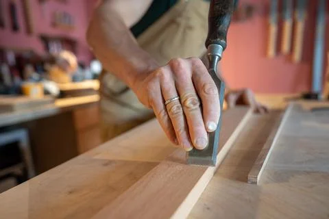 Closeup professional carpenter hand using chisel to smooth wood board surface Foto stock