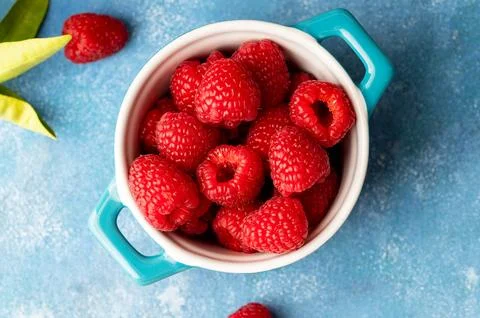 Closeup raspberry fruits in blue bowl, blue background, top view Stock-Fotos