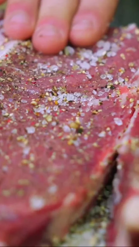 Closeup of raw beef steak being seasoned with salt and pepper by hand Stock Footage 336656782
