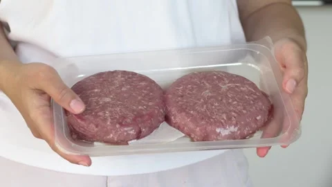 Closeup raw burger patties in packaging held by woman hands, ideal for grocery Video stock 333770426
