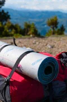 Closeup Red Backpack With sleeping mat Lays on rocky ground in front of mountain Stock Photos