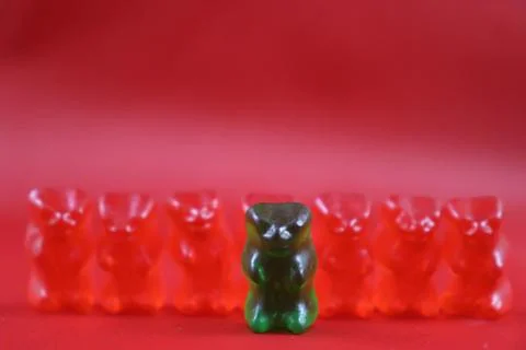 Closeup of red candy bear army with green candy bear leader isolated in red Stock Photos