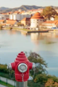 Closeup of red fire hydrant and sunlit old town by the river in background Stock Photos