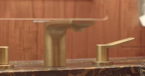 Closeup of refined marble surface with gleaming brass faucet highlight Vidéo 333892534