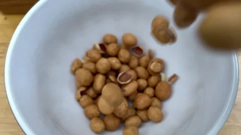 Closeup of Roasted Peanuts Falling into White Bowl on Wooden Table Stock Footage 344500017