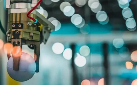 Closeup robot hand machine picking up white ball on bokeh blurred background. Stock Photos