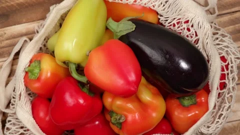 Closeup rotation of set of fresh vegetables in string bag on wooden background. Video stock 252372737