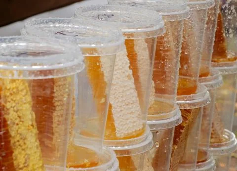 Closeup row of clear plastic cups filled with honeycomb and amber honey under Stock Photos