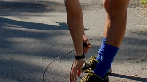 Closeup of runner adjusting shoes under warm sunlight in park Stock Footage 320955310