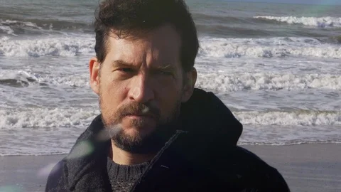 Closeup of sad man looking camera in winter in front of waves strong sea Stock Footage 118392320