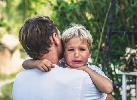Closeup Sad young blond boy crying on father hands in nature park outdoor. Man Stock Photos