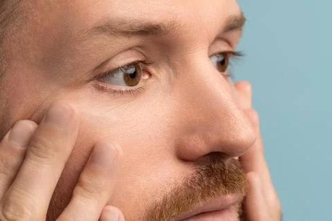 Closeup of serious bearded man looking at wrinkles under eyes touching face skin Stock Photos