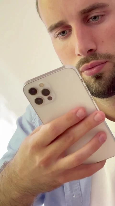Closeup of a serious young man with a beard and blue eyes using a smartphone Vídeos de archivo 344756268
