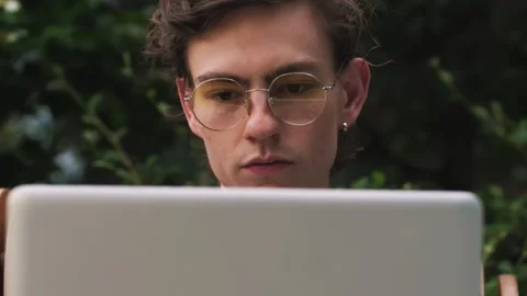 Closeup of serious young man working on laptop computer in cafe outdoors. Man Video stock 243662125