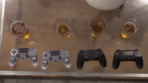 Closeup of several wireless video game controllers next to glasses of beer on Видео 193002389